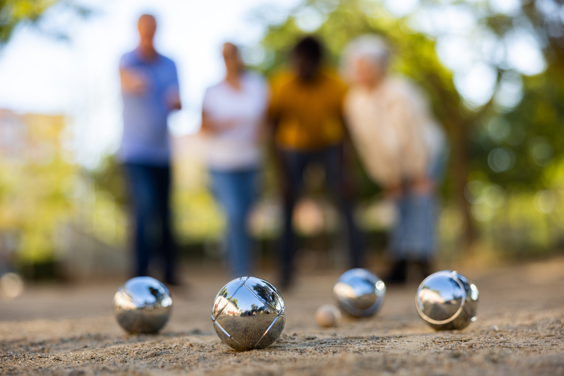 1479287040 View of petanque shiny silver metal balls laying on the ground outside in the park with group of people standing behind on a sunny day